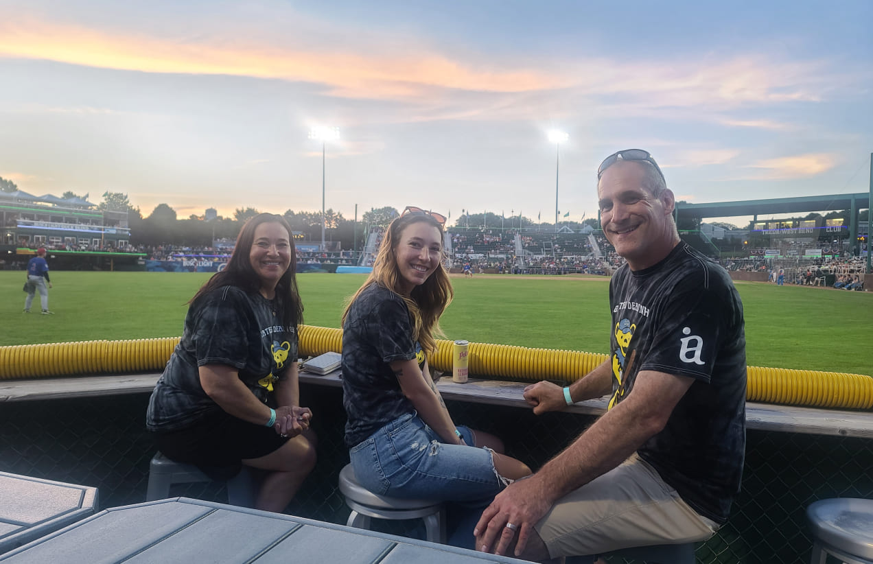 Three members of the IA team sit infront of the Milwaukee Brewers field at sunset.