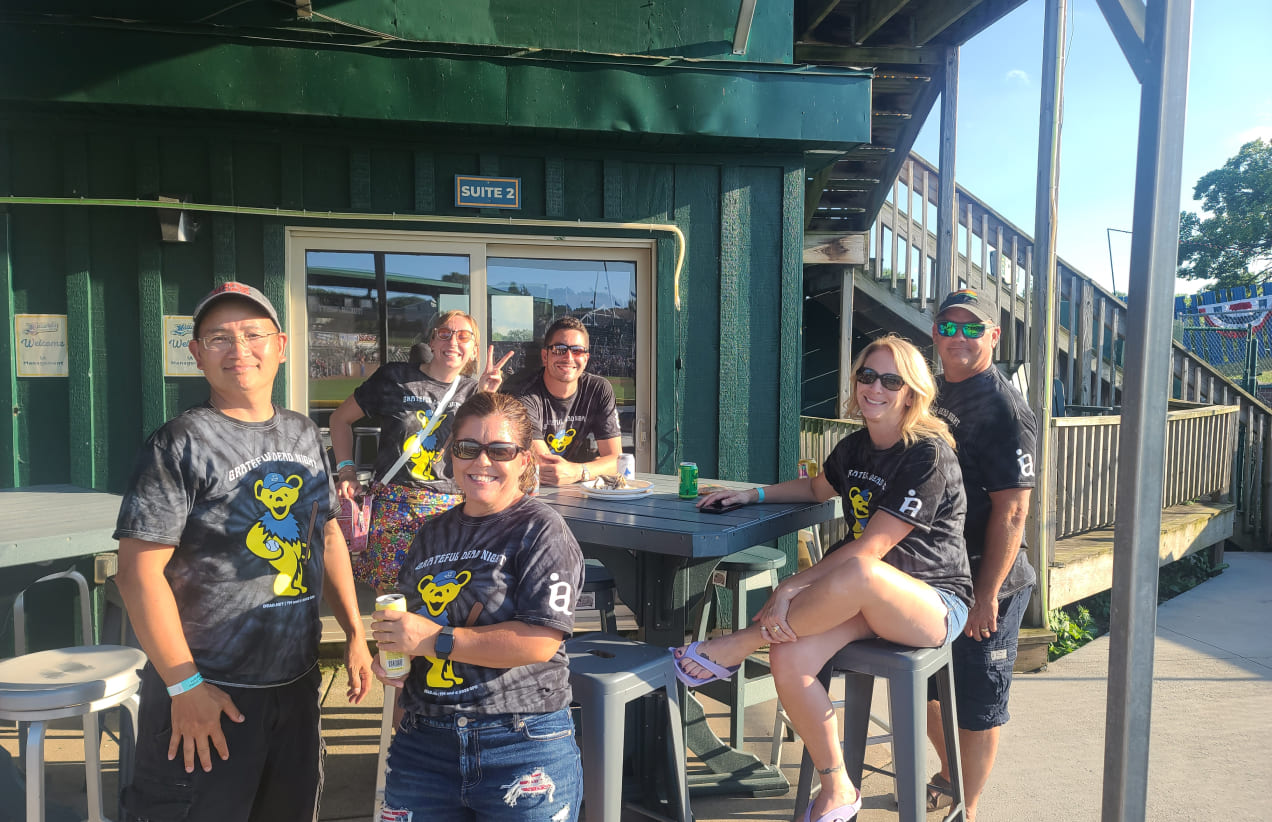 Members of the IA team sit around a picnic table enjoying food and drinks at a Brewers game.