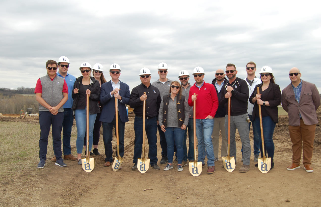 The Investors Associated team wears hard hats and holds IA-branded shovels to break ground on new construction.