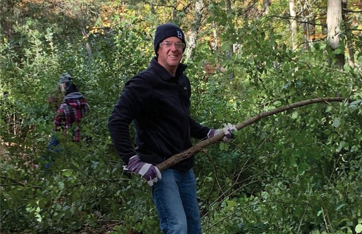 Shawn Swenson holds a large branch while volunteering in a community forest.