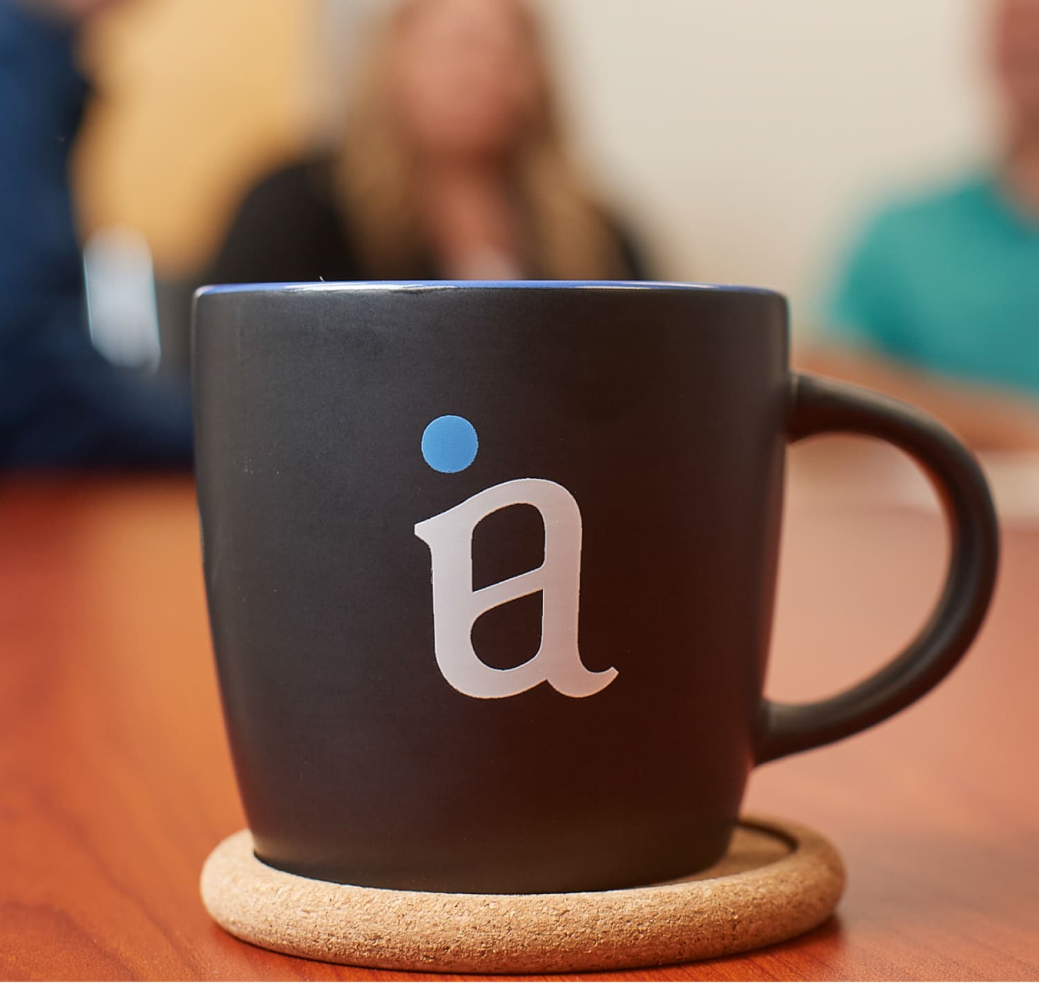 mug branded with the Investors Associated logo sits on a coaster on a table.